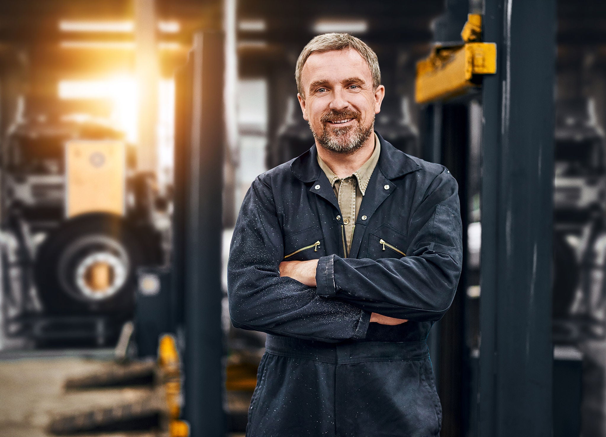 (Um sorridente dono de garagem está olhando para a câmera de sua movimentada oficina de reparação de automóveis.)